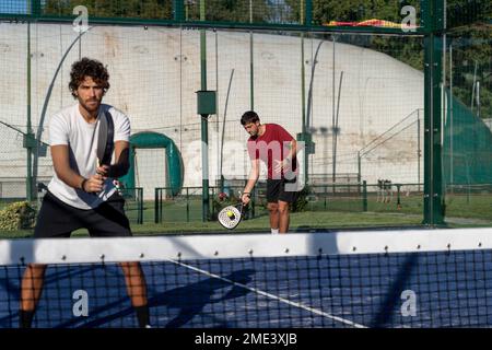 Junger Mann mit Freund, der Paddle Tennis auf dem Sportplatz spielt Stockfoto