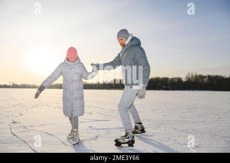 Glückliches Mädchen mit Vater, das Schlittschuhlaufen auf dem Wintersee praktiziert Stockfoto