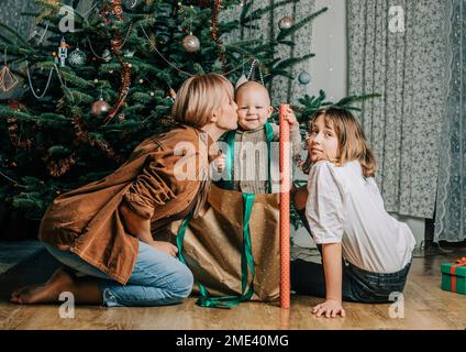 Mutter küsst Sohn mit Mädchen, die zu Hause auf dem Boden sitzt Stockfoto