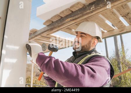 Bauarbeiter, der auf der Baustelle mit einem Hammer an der Wand arbeitet Stockfoto