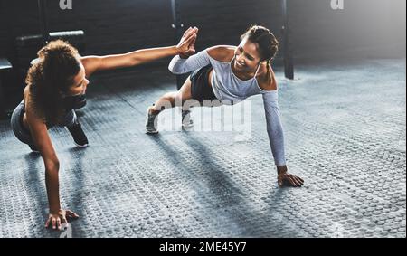 Teamwork macht das Workout zum Erfolg. Zwei junge Frauen, die sich gegenseitig High Five geben, während sie Liegestütze im Fitnessstudio machen. Stockfoto