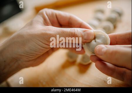 Hände einer Frau, die zu Hause Knödel in der Küche formt Stockfoto