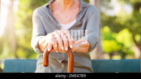 Ich kann dir ein oder zwei Dinge über das Leben erzählen. Eine nicht wiedererkennbare ältere Frau mit ihren Händen an ihrem Wanderstock draußen. Stockfoto