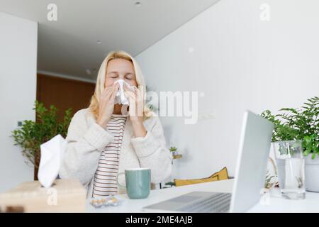 Kranker Freiberufler, der zu Hause auf Papiertüchern niest Stockfoto