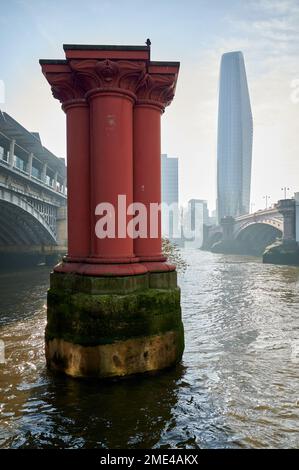 Rote Säulen oder Säulen von der ursprünglichen Blackfriars-Eisenbahnbrücke in der themse, london an einem sonnigen Tag im Winter mit einem Blackfriars-Gebäude in B Stockfoto