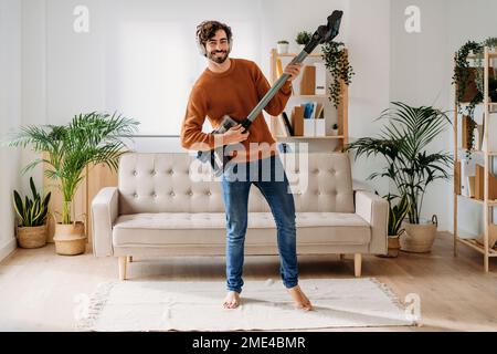 Glücklicher Mann, der zu Hause Gitarre auf dem Staubsauger spielt Stockfoto