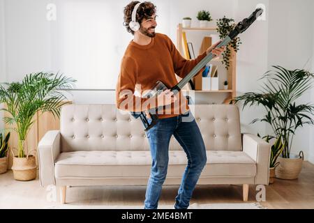 Glücklicher junger Mann, der zu Hause tanzt und Gitarre spielt Stockfoto