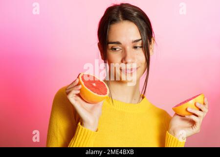 Lächelnde junge Frau mit Grapefruithälften vor pinkfarbenem Hintergrund Stockfoto