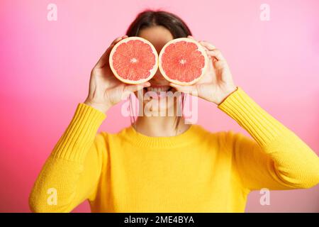 Lächelnde Frau mit Grapefruithälften vor pinkfarbenem Hintergrund Stockfoto