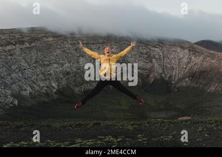 Eine sorglose Frau mit ausgestreckten Armen springt am Vulkan Caldera Blanca, Lanzarote, Kanarische Inseln, Spanien Stockfoto