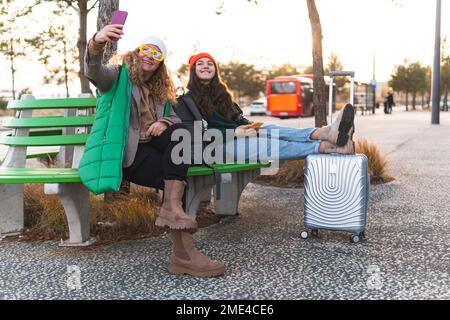 Glückliche Mutter mit Tochter, die Selfie macht, obwohl das Smartphone auf der Bank sitzt Stockfoto