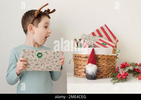 Süßer Junge, der Adventsgeschenke in einem Korb an der Wand sieht Stockfoto