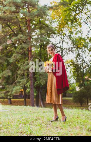 Junge Frau steht im Park mit Ahornblättern Stockfoto