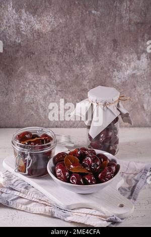 Marinierte Pflaumen mit Gewürzen im Glasgefäß auf dem Küchentisch Stockfoto