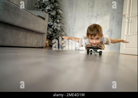 Glücklicher Junge mit ausgestreckten Armen, der zu Hause auf dem Skateboard lag Stockfoto