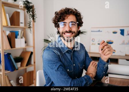 Fröhlicher junger Ingenieur mit Brille, der einen Stift im Büro hält Stockfoto