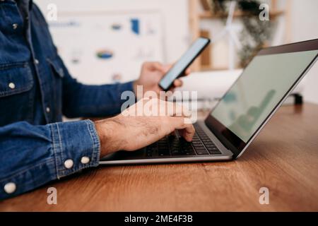 Die Hände eines Technikers, der auf dem Laptop tippt und das Smartphone im Büro hält Stockfoto