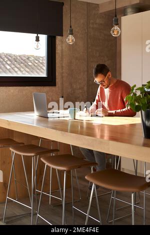 Mann, der am Schreibtisch auf Notizblock mit Stift schreibt Stockfoto