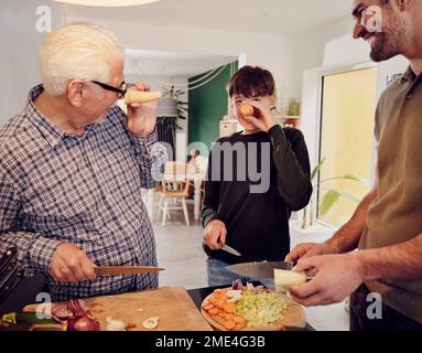 Großvater, Vater und Sohn hacken Gemüse in der Küche zusammen und haben Spaß mit Karotten Stockfoto