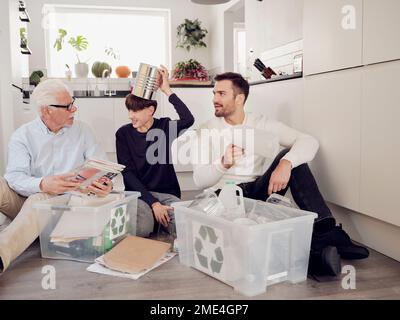 Großvater, Vater und Sohn haben Spaß dabei, Abfälle in Recyclingboxen zu trennen Stockfoto