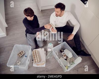 Vater und Sohn trennen Abfälle in Recyclingkisten Stockfoto