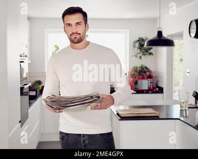 Ein Mann, der in der Küche steht und Altpapier hält Stockfoto