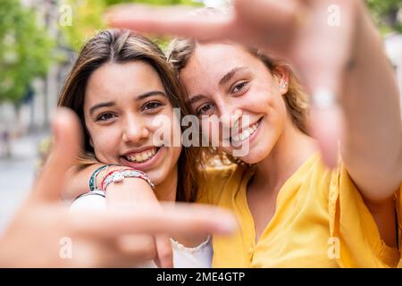 Fröhliche junge Freunde, die einen Fingerrahmen machen Stockfoto