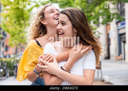 Glückliche Frau, die eine Freundin auf dem Fußweg umarmt Stockfoto