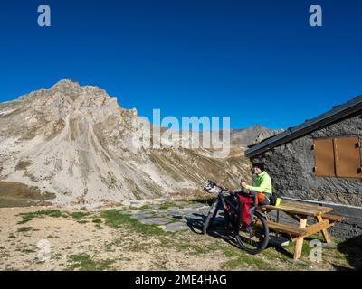 Ein älterer Mann mit einer Flasche sitzt auf einer Bank vor dem Mountainbike, Vanoise-Nationalpark, Frankreich Stockfoto