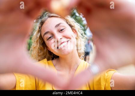 Glückliche junge Frau, die mit den Händen ein Herz geformt Stockfoto