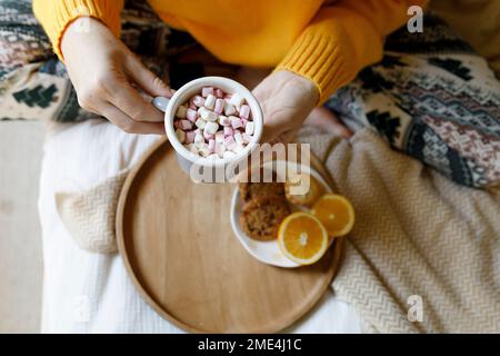 Eine Frau, die eine Tasse heiße Schokolade mit Marshmallows auf dem Bett hält Stockfoto