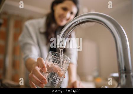Frau, die zu Hause Wasser aus dem Wasserhahn in Glas füllt Stockfoto