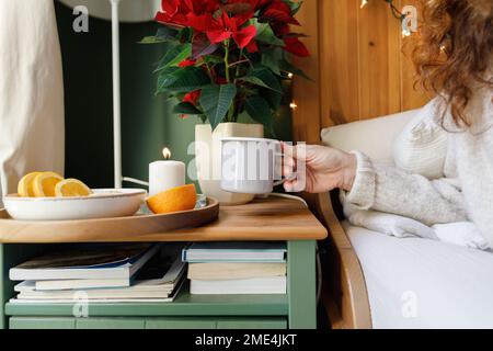 Die Hand einer Frau, die zu Hause einen Becher vom Beistelltisch nimmt Stockfoto