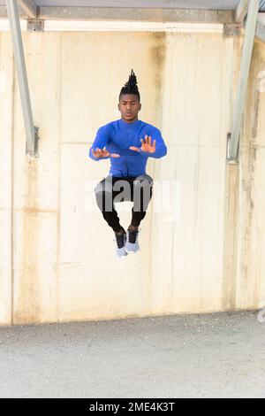 Junger Mann, der Springübungen auf dem Fußweg vor der Wand macht Stockfoto