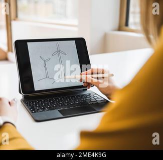 Geschäftsfrau mit digitalem Stift, die Windturbine auf Tablet-PC zeichnet Stockfoto