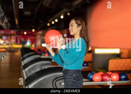 Junge Frau hält Bowlingkugel in der Gasse Stockfoto