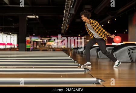 Junger Mann, der Ball auf die Bowlingbahn wirft Stockfoto