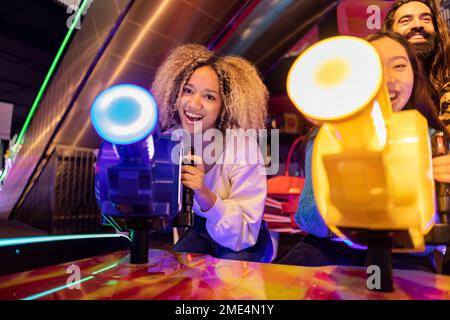 Glückliche junge Frau mit Freunden, die Videospiele in einer Spielhalle spielen Stockfoto