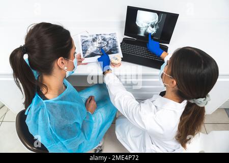 Junge Zahnärzte diskutieren über Röntgenbild und verwenden Laptop in der Klinik Stockfoto