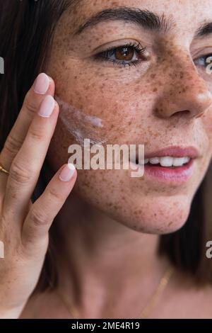 Junge Frau mit Sommersprossen, die Feuchtigkeitscreme auf das Gesicht aufträgt Stockfoto