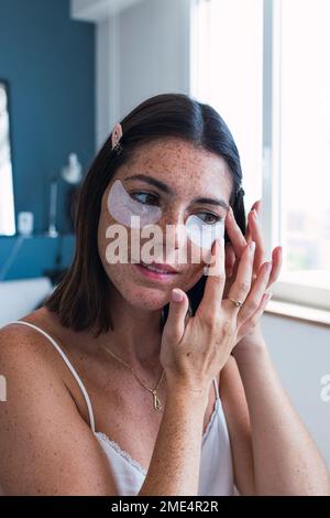 Junge Frau, die zu Hause Augenpflaster aufträgt Stockfoto