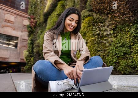 Glückliche junge Frau, die einen Tablet-PC außerhalb eines vertikalen Gartens verwendet Stockfoto