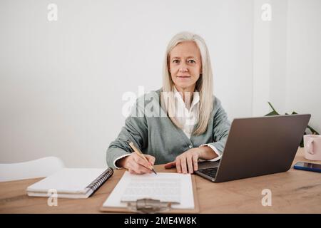 Lächelnder Freiberufler mit Dokumenten und Laptop am Schreibtisch Stockfoto