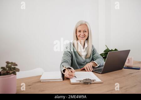 Zufriedener Freiberufler mit Dokumenten und Laptop im Home Office Stockfoto