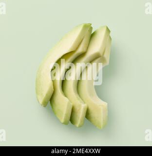 Frische rohe Avocado-Schichten auf grünem Hintergrund, Draufsicht Stockfoto