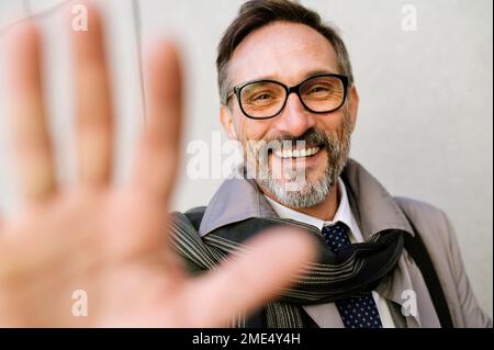 Ein glücklicher, reifer Geschäftsmann, der sich vor der Wand bewegt Stockfoto