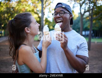 Gemischte Rassen, Eiscreme oder ein paar Freunde in einem Park, die bei einem romantischen Date in der Natur zusammen spazieren. Romantik, entspannter Schwarzer und glücklich Stockfoto