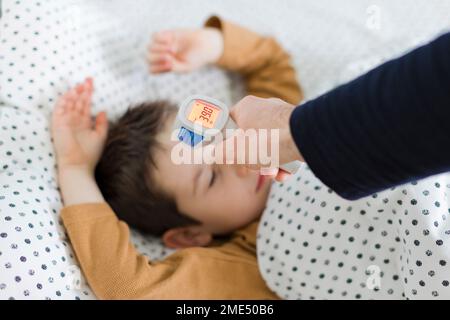 Die Hand des Vaters misst die Temperatur des zu Hause auf dem Bett liegenden Sohnes Stockfoto