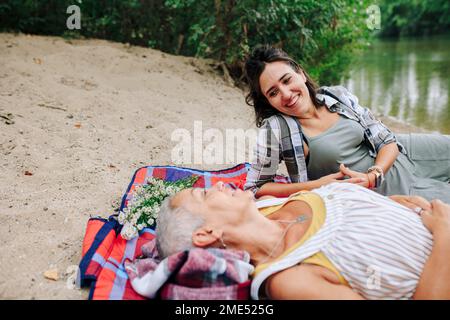 Glückliche Frauen, die sich in der Nähe des Sees im Park entspannen Stockfoto