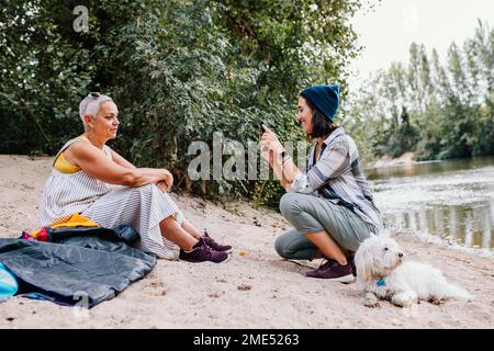 Junge Frau klickt Fotos von einem Freund mit Hund, der im Park sitzt Stockfoto